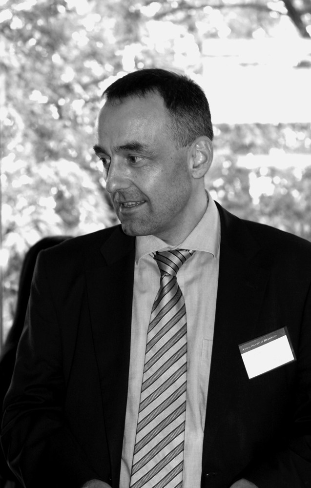 schwarz-weiß Bild von einem Mann mit Anzug und Krawatte und Brille, der nach unten schaut
